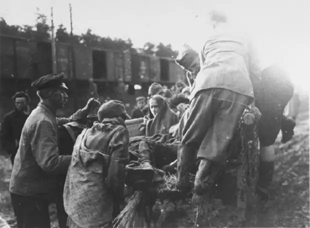 Солдат помогает обессиленному военнопленному подняться в кузов машины.