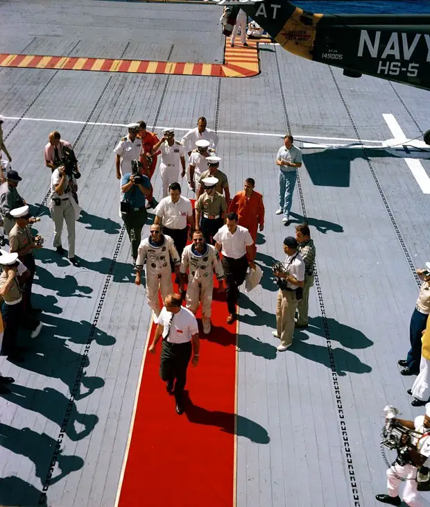 1965, 29 августа. Астронавты Л. Гордон Купер и Чарльз Конрад идут по красному ковру на борту авианосца USS Lake Champlain после приводнения