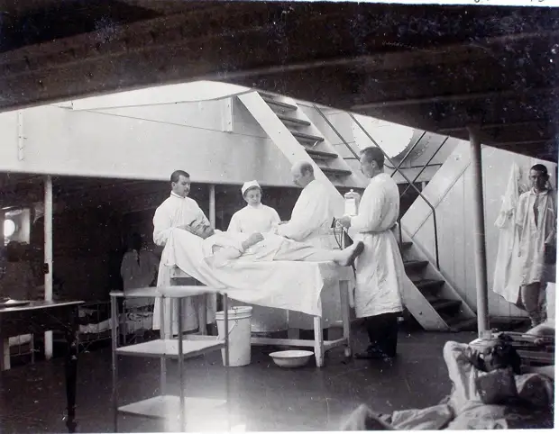 24. Старший врач И. Х. Дзирне (третий слева), сестра милосердия, младший врач В. П. Ивакин - справа крайний перевязывают больного в палате № 2 (на перевязочном пункте). 1901