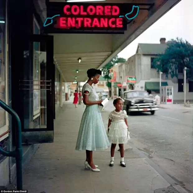 Молодая афро-американка с дочерью под указателем с надписью Вход для цветных