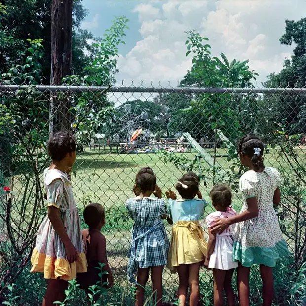 Негритянские дети толпятся и заглядывают через заграждение парка развлечений и отдыха Только для белых