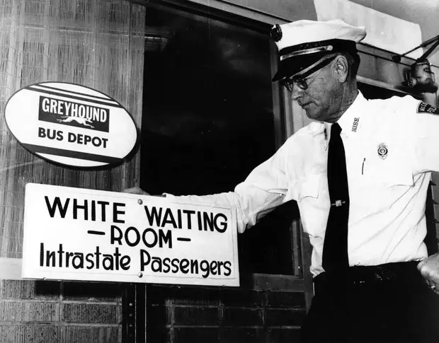 Полицейский у входа в помещение автовокзала с надписью Комната ожидания для белых
